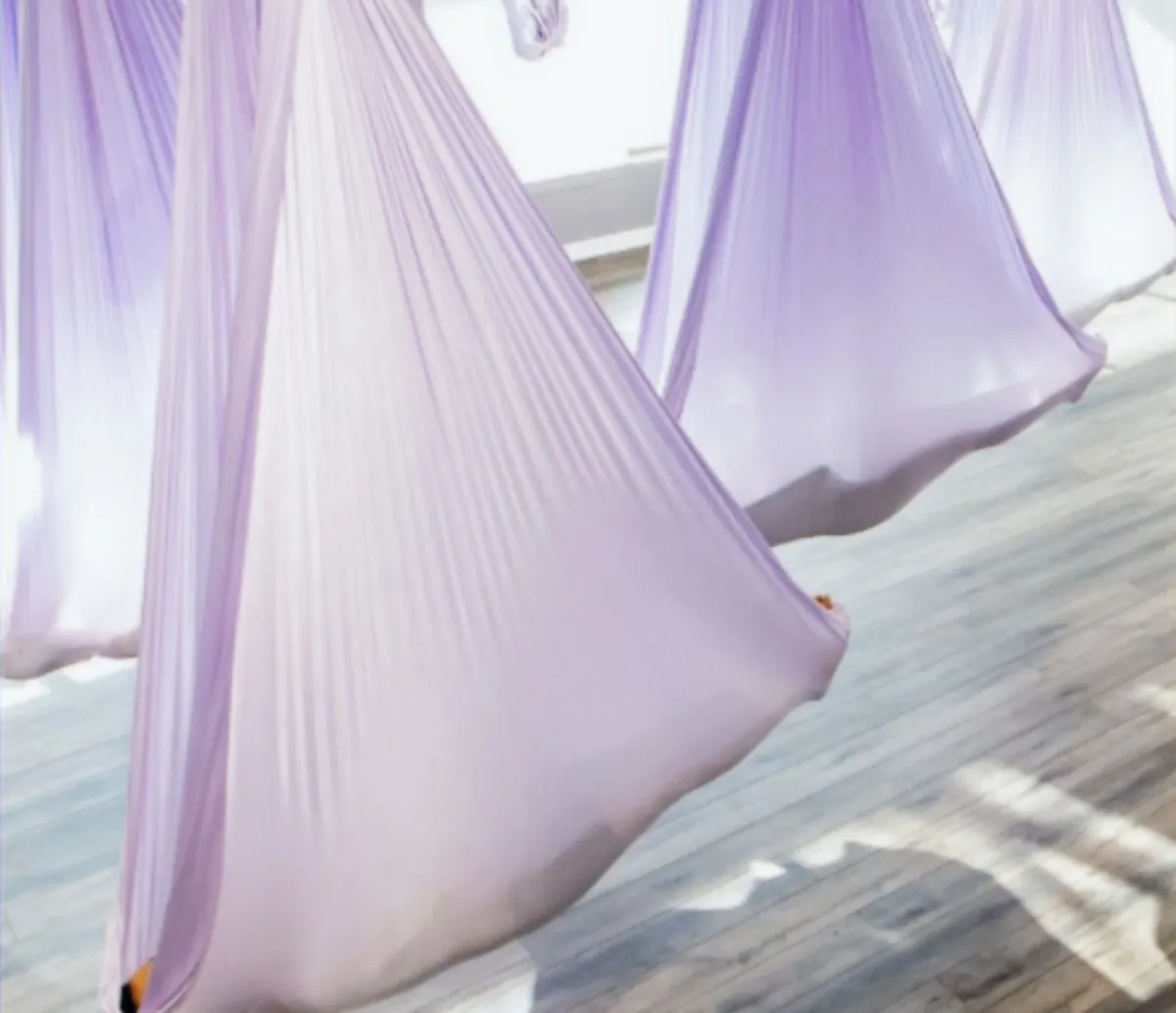 Light purple aerial yoga hammocks in a bright studio with wooden floors